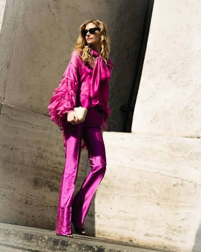 Portrait of Sveva Clavarino in a fuchsia silk ensemble, standing against a stone facade.